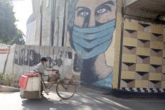 Life goes on: A food vendor pushes his laden bicycle past a coronavirus-themed mural of a health worker in Tebet, South Jakarta on Jan. 9, 2021. The prolonged pandemic does not affect people’s spirit to remain active. (Courtesy of JADIGUNAImages/Jerry Adiguna)
