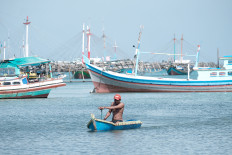 A man rows a dinghy to shore between several anchored traditional fishing boats in this undated photograph.