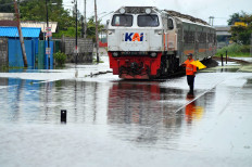 A rail worker guides a train along flooded tracks in Semarang, Central Java, on Friday.