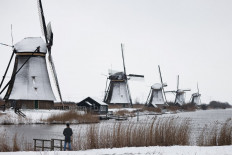 Snow blankets a field as a man stands in front of windmills in the village of Kinderdijk, on February 7, 2021. The Netherlands was blanketed on February 7 by the first major snowstorm to hit the country in 10 years, disrupting rail and road traffic, as a cold front pushed through northern Europe. The Dutch meteorological agency KNMI declared a rare 