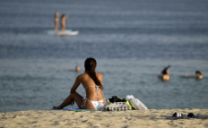  In this file photo taken on July 24, 2020, a woman sunbather sits along a beach as people stand up paddle board in the water in the Gulf emirate of Dubai. In Dubai, known for its luxury haunts and parties, expatriate singles working in the city find the quest for a partner difficult. 