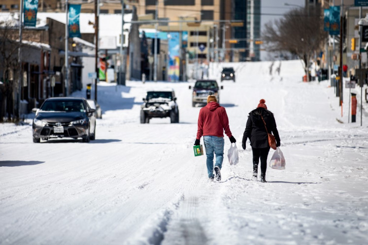People carry groceries from a local gas station on February 15, 2021 in Austin, Texas, US. Winter storm Uri has brought historic cold weather to Texas, causing traffic delays and power outages, and storms have swept across 26 states with a mix of freezing temperatures and precipitation. 