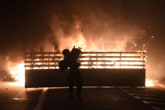 A protester throws a stone into flames during clashes with Catalan regional forces Mossos d'Esquadra after a demonstration against the arrest of Spanish rapper Pablo Hasel in Barcelona on February 16, 2021. Spanish police stormed a university to arrest the rapper barricaded inside after being sentenced to nine months' jail over tweets attacking the monarchy and the police in a case denounced as an attack on freedom of speech.