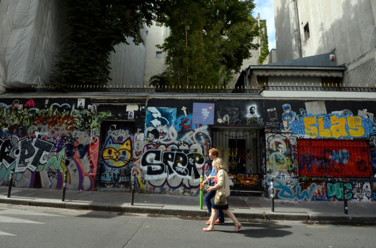 People walk past the graffiti-covered house of late French singer and songwriter Serge Gainsbourg in central Paris on July 22, 2015. 