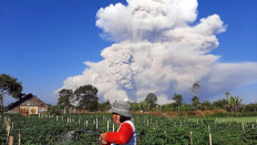A farmer tends to a farm as Mount Sinabung spews ash into the sky, as seen from Karo, North Sumatra on March 2, 2021. 