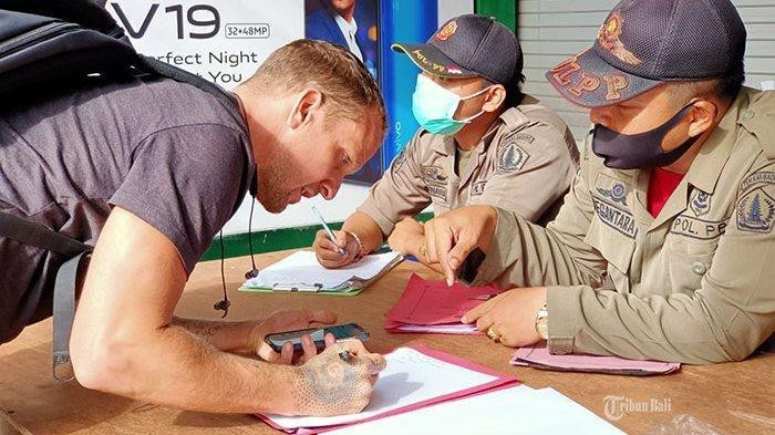 Local law enforcement officers collect a fine from a foreign man caught not wearing a mask while riding a motorcycle in Bali, Indonesia's top tourist destination.