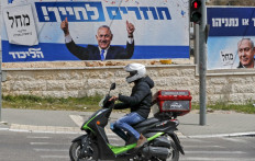 A motorcyclist rides past a campaign poster of Israeli Prime Minister Benjamin Netanyahu, in Jerusalem on March 22, 2021.
