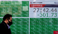 A pedestrian wearing a face mask walks past a stock indicator displaying numbers of Nikkei 225 of the Tokyo Stock Exchange in Tokyo on January 4, 2021, on the first trading day of the year.
