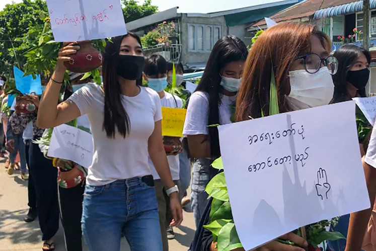 Protesters carry pots filled with Thingyan festival flowers and leaves as they hold signs during a demonstration against the military coup in Yangon on April 13, 2021. 