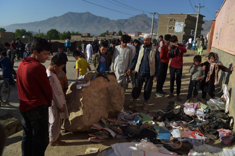 Onlookers stand next to a pile of backpacks and books of victims following yesterday's multiple blasts outside a girls' school in Dasht-e-Barchi on the outskirts of Kabul on May 9, 2021, as the death toll has risen to 50, the interior ministry said. 