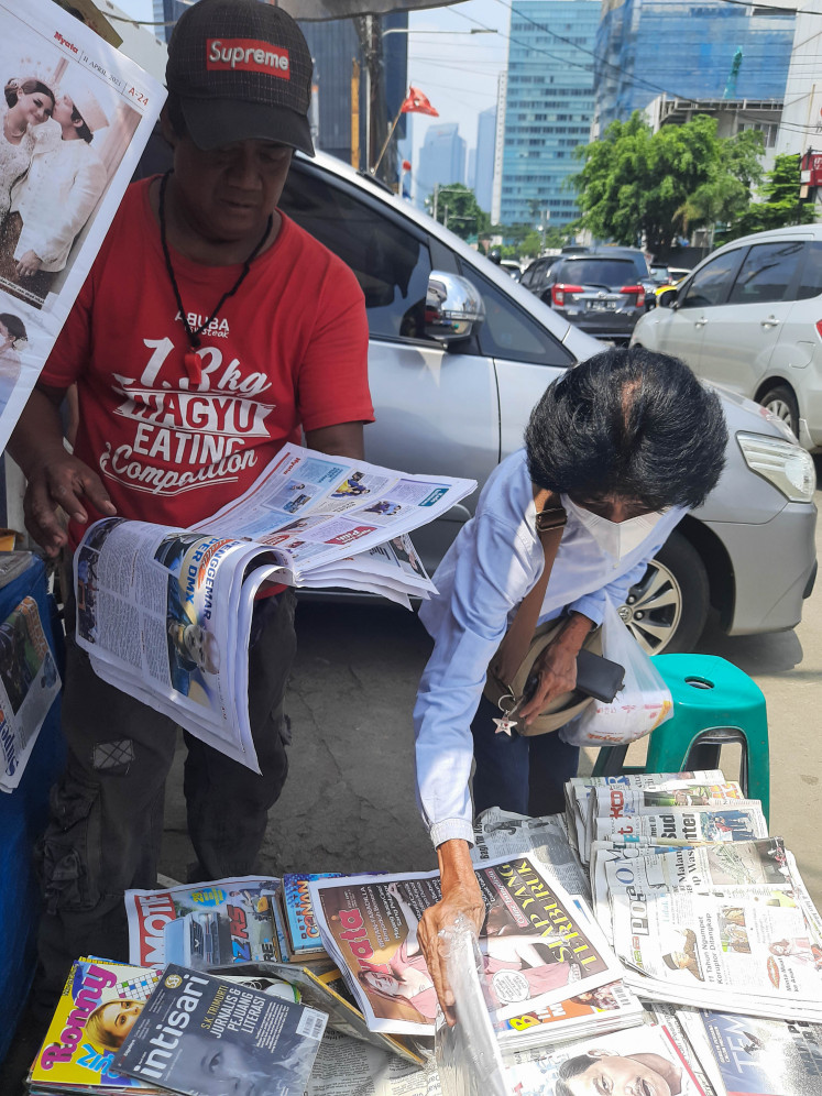 Lifeblood: Iwan sells a newspaper to a passerby. He says he will keep selling newspapers and magazines for as long as he can.