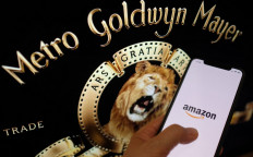 This illustration photo taken May 26, 2021, shows the Amazon logo on a smartphone in front of the MGM lion. Amazon has agreed to buy the storied MGM studios for $8.45 billion, giving the US tech giant a vast library to further its ambitions in streaming.