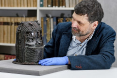 A handout picture taken on March 17, 2021 at the University of Aberdeen shows Neil Curtis, Head of Museums and Special Collections posing by a bronze sculpture depicting an 