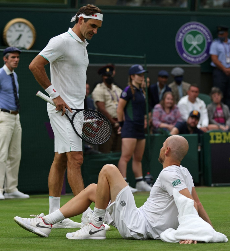 Switzerland's Roger Federer (2L) talks to France's Adrian Mannarino after Mannarino slipped on the grass during their men's singles first round match on the second day of the 2021 Wimbledon Championships at The All England Tennis Club in Wimbledon, southwest London, on June 29, 2021. Mannarino withdrew from the match due to injury.