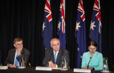 Australian Prime Minister Scott Morrison (center) sits between Brendan Murphy (left), Chief Medical Officer of Australia, and the Premier of New South Wales Gladys Berejiklian, during a media conference after the Meeting of the Council of Australian Governments (COAG) at Parramatta Stadium, in western Sydney on March 13, 2020. 