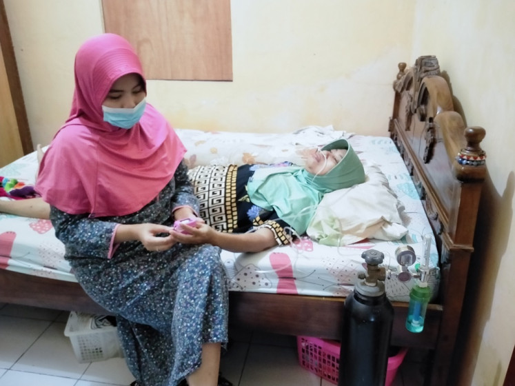 Rita Octavia (left) checks her mother’s oxygen level on July 9, 2021 at the family home in Bantul regency, Yogyakarta. Rita and her family have all tested positive for COVID-19 and are self-isolating, even though her mother needs medical treatment because she has comorbid diabetes. 