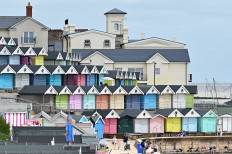 People walk along the promenade past beach huts at Walton-on-the-Naze, in southeast England on July 15, 2021. Brightly painted wooden beach huts line England's coastline and have enjoyed a boom during the pandemic, as people rediscover seaside breaks close to home.
