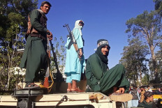 In this picture taken on August 13, 2021, Taliban fighters stand on a vehicle along the roadside in Herat, Afghanistan's third biggest city, after government forces pulled out the day before following weeks of being under siege. 