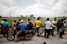 Residents look on as workers receive humanitarian aid from a US military helicopter at Les Cayes airport after Saturday's 7.2 magnitude earthquake, in Les Cayes, Haiti, August 18, 2021. 
