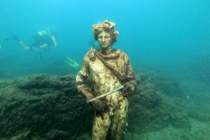 In this photograph taken on August 18, 2021 a dive guide shows tourists a copy of the original statue preserved at the Museum of Baiae, representing Dionysus with ivy crown in the Nymphaeum of punta Epitaffio, the submerged ancient Roman city of Baiae at the Baiae Underwater Park.
