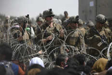 United States soldiers stand guard behind barbed wire as Afghans sit on a roadside near the military part of the airport in Kabul on Aug. 20, hoping to flee from the country after the Taliban's takeover of Afghanistan.