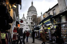 In this file photo taken on November 30, 2018 people walk past shops in a street below the Sacred Heart (sacre coeur) basilica on the Montmartre hill in Paris.