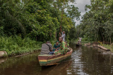 Women are ferried on a canoe through the Lokoli forest on July 9, 2021. In this forest, named after the Hlan river which crosses it, more than 241 plant and 160 animal species, including the rare red-bellied monkey, the swamp mongoose and the sitatunga, have been counted.