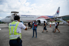 A ground staff member (left) helps to take pictures of a passenger after he disembarked from a Malaysia Airlines Boeing 738 aircraft upon its landing in Langkawi from Kuala Lumpur International Airport on September 16, 2021, as the holiday island reopened to domestic tourists following closures due to restrictions to halt the spread of the Covid-19 coronavirus. 
