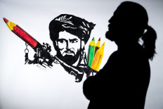 In this file photo taken in Paris on September 11, 2021 Afghan artist and co-founder of the ArtLords collective, Farshad, poses next to a symbolic drawing of his collective, representing a Taliban fighter whose rocket launcher is filled with pencils.