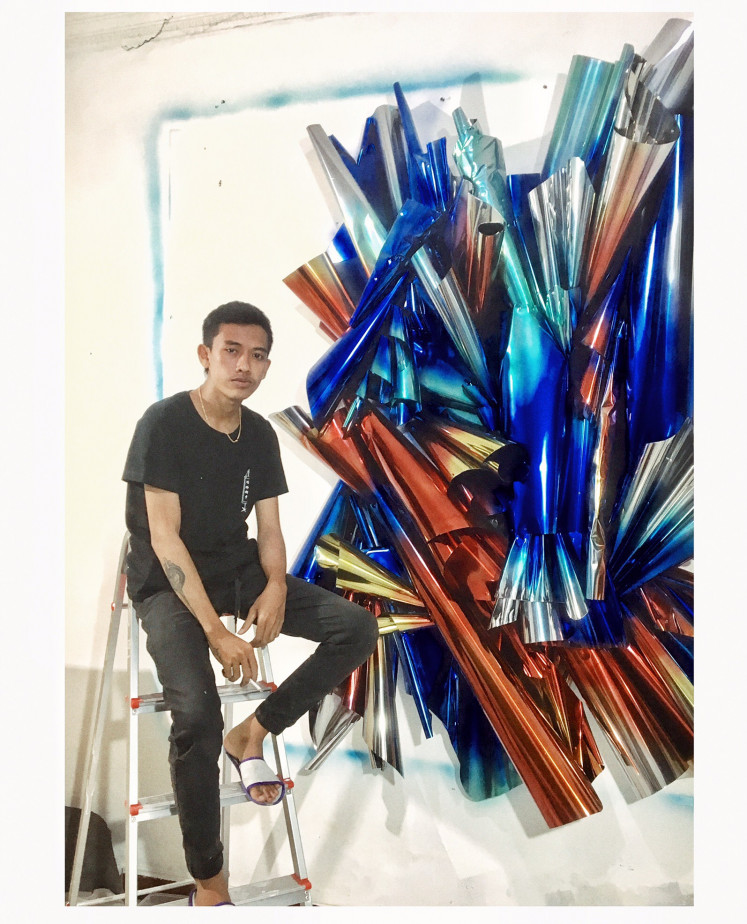 Galactic birth: I Kadek Didin Junaedi, who is better known as Didin Jirot, sits next to a piece that displays his iconic artistic style using metal sheets at his studio in Yogyakarta. (Didin Jirot)