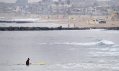 A surfer stands in the water on October 7, 2021 in Newport Beach, California, as cleanup crews (back) continue to work after an oil spill.