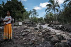 A woman stands near damaged homes in the village of Kamar Kajang in Lumajang on December 9, 2021, after the eruption of Mount Semeru volcano on December 4 killed at least 39 people. 