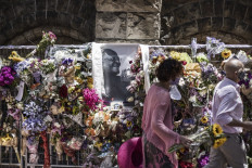 A woman carries a flower bouquet past a portrait of South African anti-apartheid icon Archbishop Desmond Tutu seen on the wall of remembrance outside the St George's Cathedral in Cape Town, on December 31, 2021.