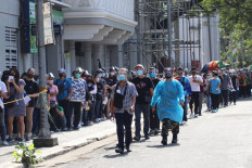 A health worker (R) walks past people queueing up for Coronavirus swab tests outside a gymnasium in Manila on January 7, 2022, as infections driven by the Omicron variant have tripled in the last two days in the nation's capital. 
