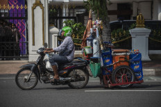 A vendor pulls his cart with a motorcycle along a street in Surabaya on Nov. 22, 2021.