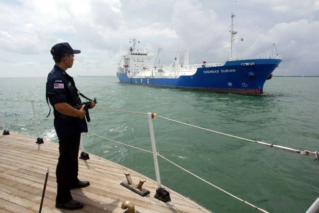 A Malaysian armed marine policeman stands guard on July 3, 2003, on the deck of his patrol boat while patrolling past a tanker in the Strait of Malacca. 