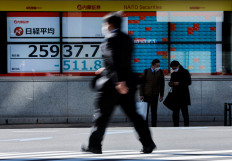 Passersby wearing protective face masks walk past a stock quotation board in Tokyo on Feb. 24, 2022.