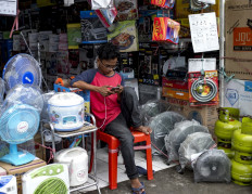A young man plays with his smartphone while waiting for customers in front of his electronics shop in Jakarta on Jan. 19, 2018.
