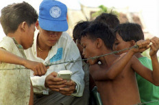 Children look on as a Cambodian UNTAC election worker plays a pocket-size computer game during a break 27 May at a mobile polling station in the outskirts of the Cambodian capital. Most of Cambodia's provinces were quiet 27 May as turnout reached 86 percent of the country's 4.7 million registered voters with only two days of polling left.