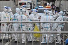 Officials and workers, wearing protective gear, work in an area where barriers are being placed to close off streets around a locked down neighbourhood after the detection of new cases of COVID-19 in Shanghai on March 15, 2022. 