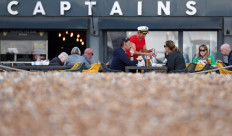 Fish and Chip shop owner Pam Sandhu (4R) serves customers as they sit and eat lunch outside of Captain's Fish and Chips shop in Brighton on March 25, 2022.