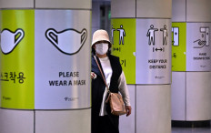 A woman walks past posters showing precautions against the Covid-19 coronavirus at a subway station in Seoul on April 15, 2022.