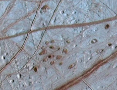 This image obtained 31 October, 2002 shows reddish spots and shallow pits peppering the enigmatic ridged surface of Jupiter's moon Europa in this composite view captured by NASA's Galileo spacecraft during two different orbits around Jupiter. The spots and pits visible in this region of Europa's northern hemisphere are each about 10 kilometers (6 miles) across. The dark spots are called 