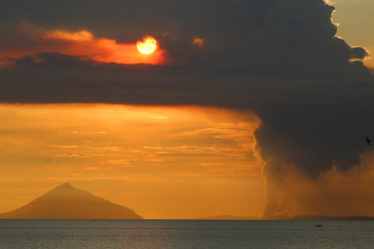 The sun sets on the backdrop as Mount Anak Krakatau (right) spews thick smoke, in this file photo taken on April 24, 2022, as seen from Pasauran beach, Anyer in Serang, Banten.