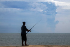 A man fishes on April 24, 2022, at Pasauran beach, Serang, Banten, while Mount Anak Krakatau spews thick smoke into the air. 