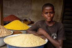 A young boy poses next to some rice in his shop at Ajara Market in Badagry, near Lagos, on September 6, 2019. The days of heaping 50-kilo sacks of rice across the saddle of their motorbike and slipping a few notes to a customs officer are now gone. With Nigeria having snapped its borders shut, the legions of motorbike riders who used to satisfy the nation's hunger for imported rice are lucky at best to sneak through a few packets of Basmati.