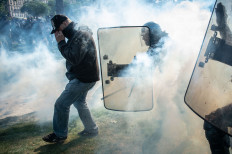 A police officer clashes with a protesters in tear gas smoke on the sidelines of the annual May Day (Labor Day) rally, marking International Workers' Day, in Paris on May 1, 2022.