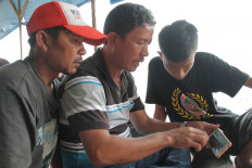 A man holds a smartphone looking at social media images as he waits for news on a boat accident in North Sumatra on June 21, 2018.