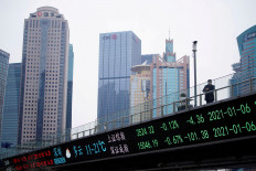 A man stands on an overpass with an electronic board showing Shanghai and Shenzhen stock indexes, at the Lujiazui financial district in Shanghai, China, on Jan. 6, 2021. 