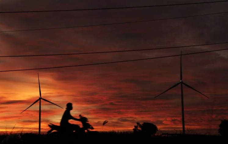 Blowing in the wind: A local resident rides his motorbike past a wind power plant facility in Tolo district, Jeneponto regency, South Sulawesi, on March 25, 2022.